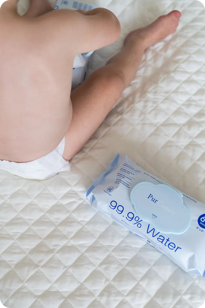 Baby on quilted bedding beside a pack of wipes